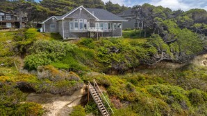 Ein Küstenhaus mit einer Treppe, die zu einer Terrasse führt, umgeben von dichter Vegetation und Hügeln.