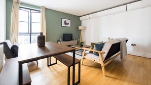 A modern living room with a wooden floor, a sofa, a coffee table, and a TV. - The Dalston Apartments (London)