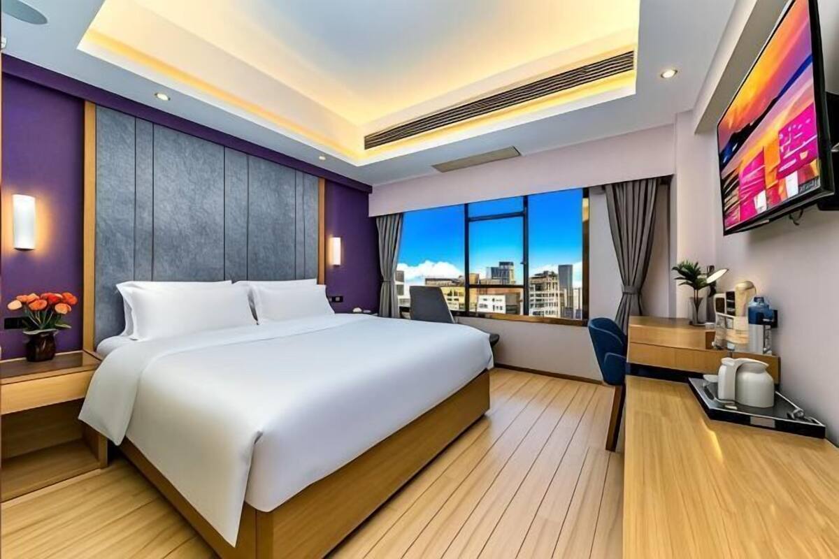 A modern hotel room with a large bed, a desk, a TV, and a city view.