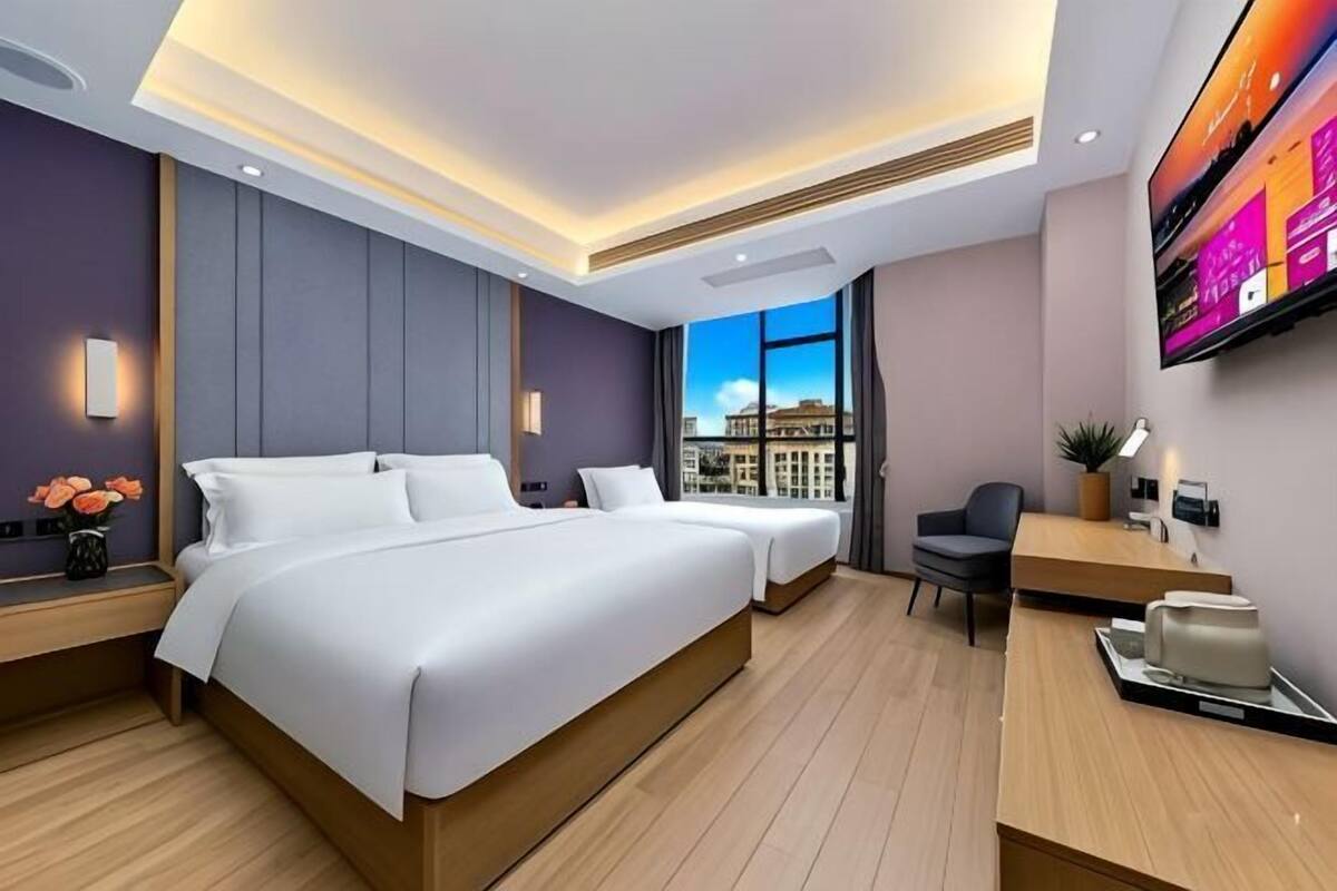 A modern hotel room with a large bed, a desk, a chair, a TV, and a view of the city.