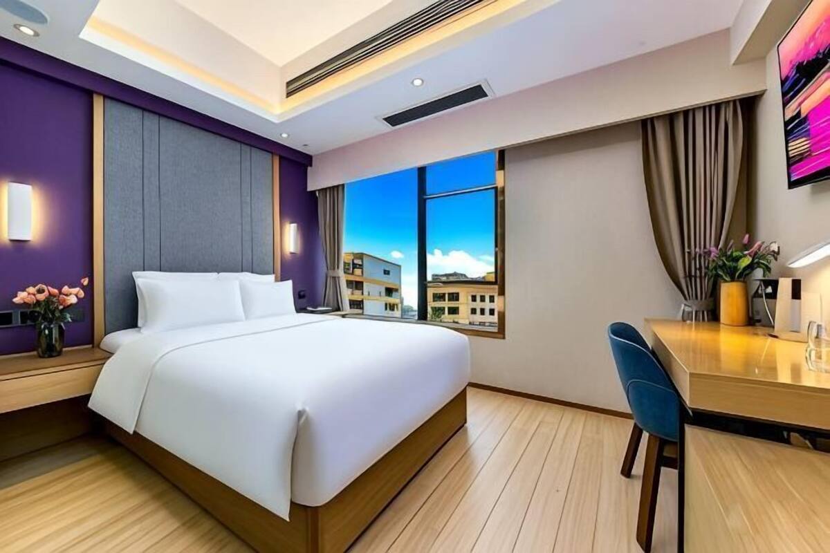 A modern hotel room with a large bed, a desk, and a city view.