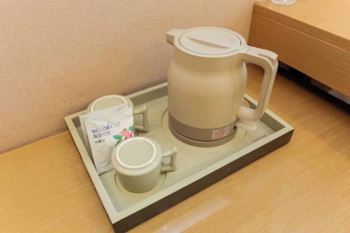 A coffee maker with a tray, a cup, and a packet of tea on a wooden table.