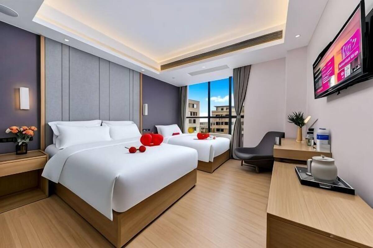 A modern hotel room with two beds, a desk, a chair, a TV, and a city view.