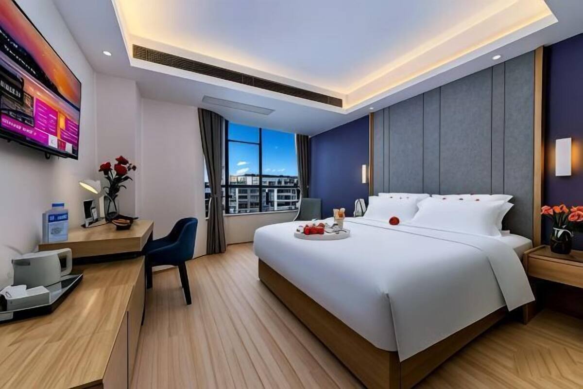 A modern hotel room with a large bed, a desk, a TV, and a city view.