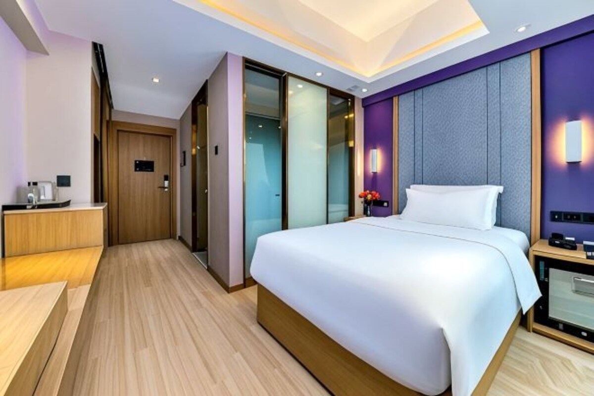 A modern hotel room with a large bed, a desk, and a walk-in closet.