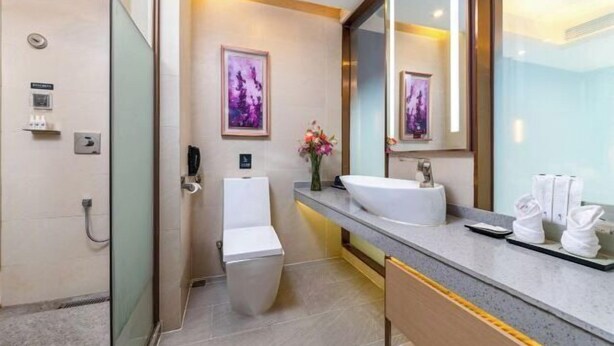 A modern bathroom with a glass shower enclosure, a white toilet, a sink with a mirror, and a vase with flowers. - Lavande Hotel (Shenzhen Airport Fuyong Metro Station) (Shenzhen)