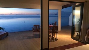 Una habitación con vista al mar, una zona de comedor con sillas y una mesa, y una cama.