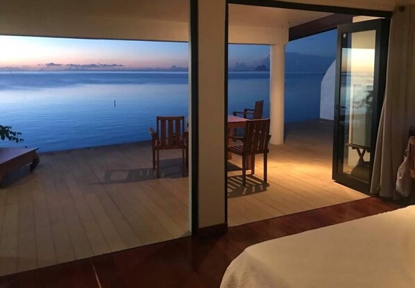 A room with a view of the sea, a dining area with chairs and a table, and a bed.