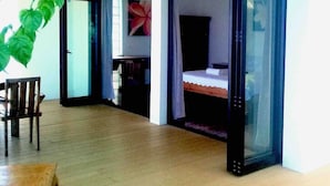 Una habitación con piso de madera, una cama, un escritorio y una silla. Hay un ventanal con cortinas.