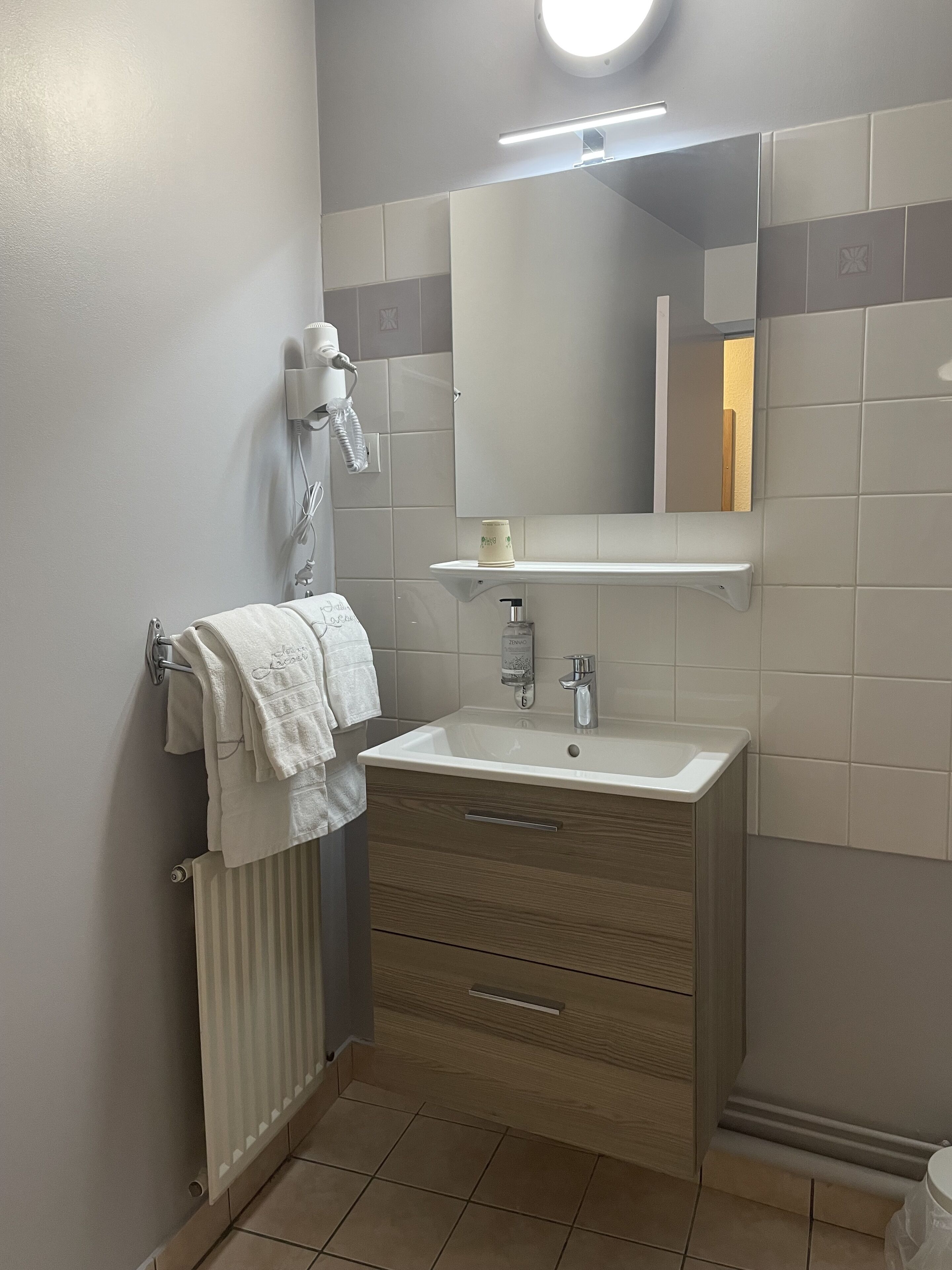 A modern bathroom with a white sink, a mirror, a towel rack, and a hairdryer.