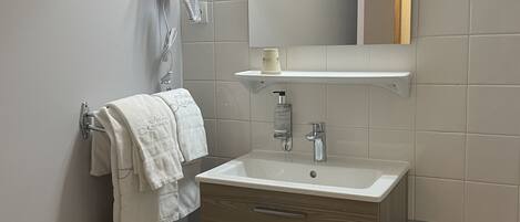 A modern bathroom with a white sink, a mirror, a towel rack, and a hairdryer.