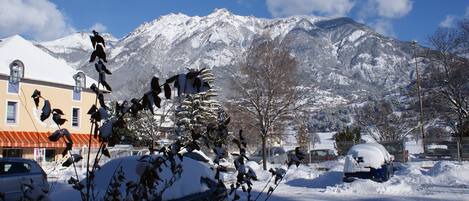 A snowy landscape with a mountain in the background, a building with a red roof, and parked cars.