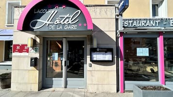 Entrada de um hotel com um arco rosa e uma placa com a inscrição 'Hotel de la Gare'.