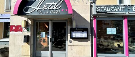 Entrada de um hotel com um arco rosa e uma placa com a inscrição 'Hotel de la Gare'.