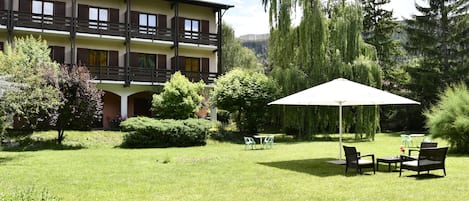 A hotel with a two-story building, outdoor seating area with chairs and a table, and a large umbrella.