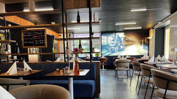 En modern restauranginteriör med trähyllor, en menytavla och ett stort fönster med utsikt över ett tåg.