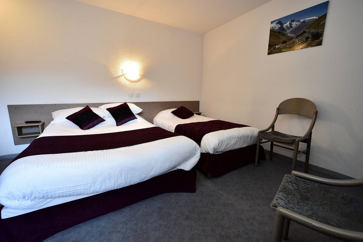 Une chambre d’hôtel avec deux lits, une chaise, une table de chevet et une lampe fixée au mur.