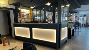 Ett välkomnande område med modern design, med en receptionsdisk med upplysta paneler, en sittgrupp med ett runt bord och stolar samt en synlig bardisk i bakgrunden.