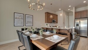 A modern kitchen with wooden cabinets, a stainless steel refrigerator, and a dining area with a wooden table and black chairs.