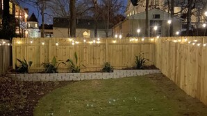 A backyard with a wooden fence, string lights, and a grassy lawn. - 5min-Grant park|Fenced Yard|Parking|Fire Pit&BBQ (Atlanta)