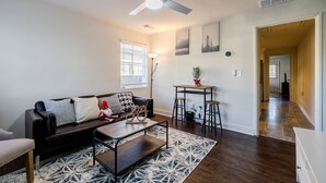 A living room with a dark brown sofa, a coffee table, and a ceiling fan. There is a window with blinds, a lamp, and a small table with a plant. - 5min-Grant park|Fenced Yard|Parking|Fire Pit&BBQ (Atlanta)