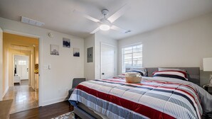 A bedroom with a large bed, a ceiling fan, a window with blinds, and a hallway leading to another room. - 5min-Grant park|Fenced Yard|Parking|Fire Pit&BBQ (Atlanta)