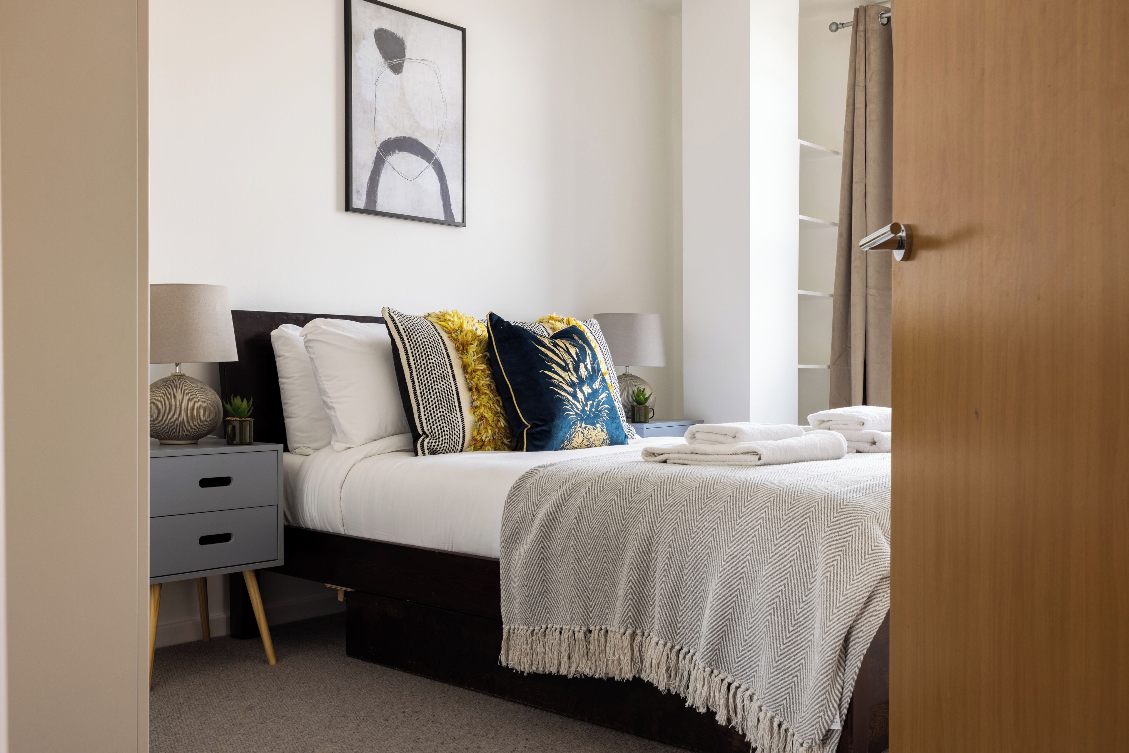 A neatly arranged bedroom with a bed, bedside tables, a lamp, and a door.