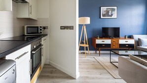 A modern kitchen with a microwave, oven, and cabinets. There is a dining area with a table and chairs, and a living room with a sofa and a TV. - Beautiful Canal-Side Apartment in Islington (London)
