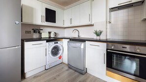 A modern kitchen with white cabinets, a built-in washing machine, a dishwasher, and an oven. - Beautiful Canal-Side Apartment in Islington (London)