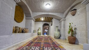 A hallway with patterned carpet, stone walls, and decorative vases. - Underground Cave Suites (Avanos)