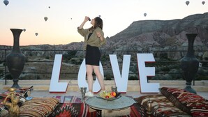 A person standing in front of a large 'LOVE' sign with hot air balloons in the background. - Underground Cave Suites (Avanos)