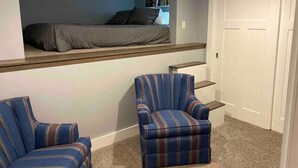 Une pièce avec un lit en hauteur, une chaise et une porte.