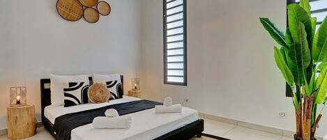 Une chambre moderne avec un lit noir, du linge de lit blanc et une grande plante en pot.