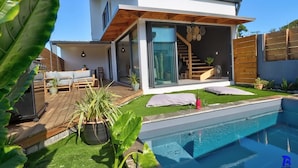 Una casa moderna con piscina, terrazza in legno e porta a vetri che dà su una scala.