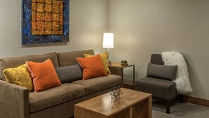 Sala de estar com sofá, poltrona, mesa de centro, abajur e obra de arte.
