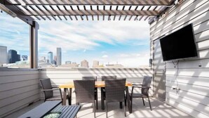 Eine Dachterrasse mit Tisch und Stühlen, einem Wand-Fernseher und Blick auf die Stadtlandschaft.