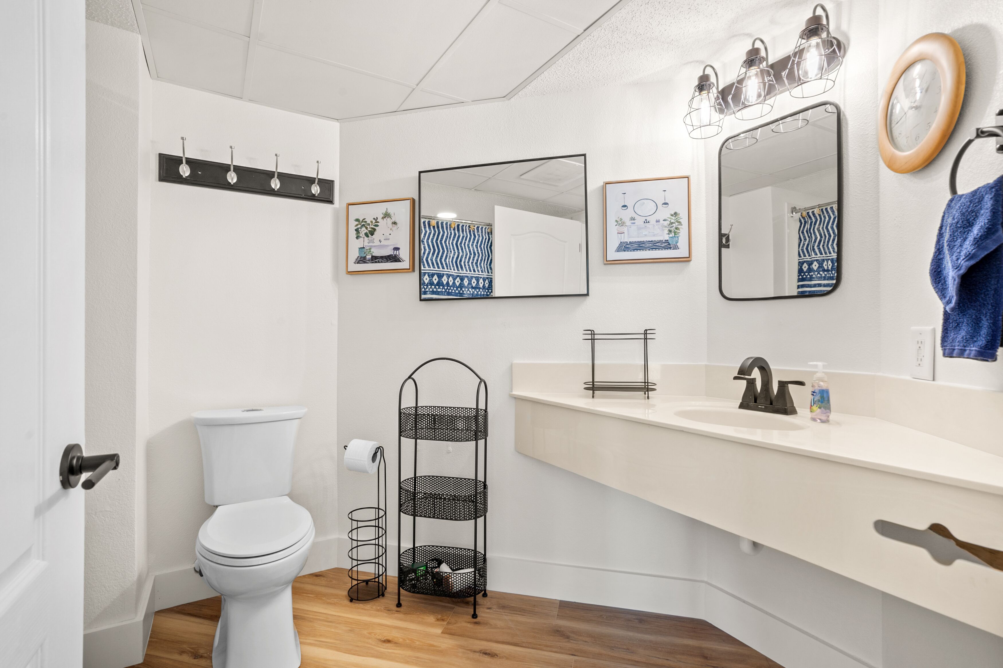A bathroom with a toilet, sink, and mirror. There are framed pictures on the wall and a towel rack.