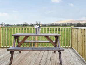 Eine Holzterrasse mit einem Picknicktisch und einem Metall-Eimer, der mit Flaschen und Gläsern gefüllt ist.