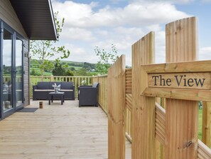 Eine Holzterrasse mit einem Schild mit dem Schriftzug 'The View', Gartenmöbeln und einer malerischen Landschaft im Hintergrund.
