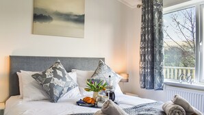 A neatly made bed with pillows, a bedside table with a lamp, a window with curtains, and a painting on the wall. - 3 bedroom accommodation in Barrow, near Clitheroe (Barrow, near Clitheroe)