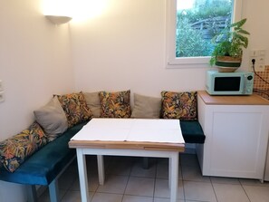 Un espace de vie compact comprenant un canapé, une petite table, un four à micro-ondes et une plante en pot.