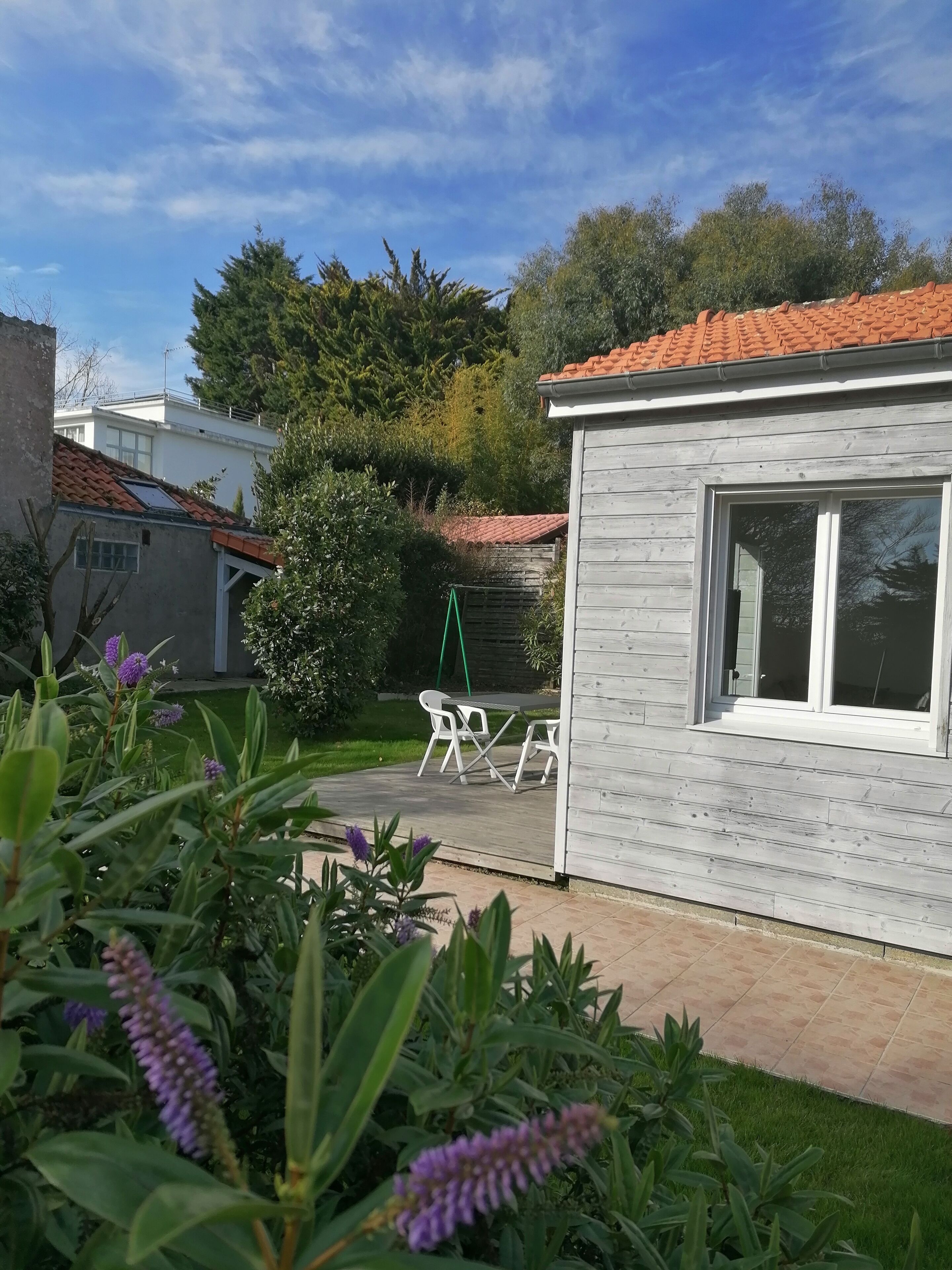 Ein Wohngebiet mit einem Haus, das ein Ziegeldach, eine Terrasse mit Gartenmöbeln und einen Garten mit violetten Blumen hat.