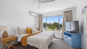 A hotel room with a bed, a desk, a television, and a window with a view of the outside. - Breakers 4 - Bright spacious apartment in the heart of Mollymook (Mollymook)