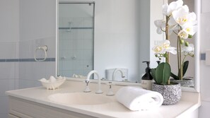 Une salle de bain avec un lavabo blanc, deux robinets, un miroir, une serviette et une bouteille de shampoing.