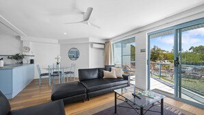 A modern living room with a black leather sofa, a glass coffee table, and a dining area with a round table and chairs. - Breakers 4 - Bright spacious apartment in the heart of Mollymook (Mollymook)