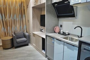 A modern kitchen with a built-in microwave, a sink, and a small seating area with a chair and a side table. - Haitao Hotel (Zhaoqing Seven Star Rock Archway Scenic Spot) (Zhaoqing)