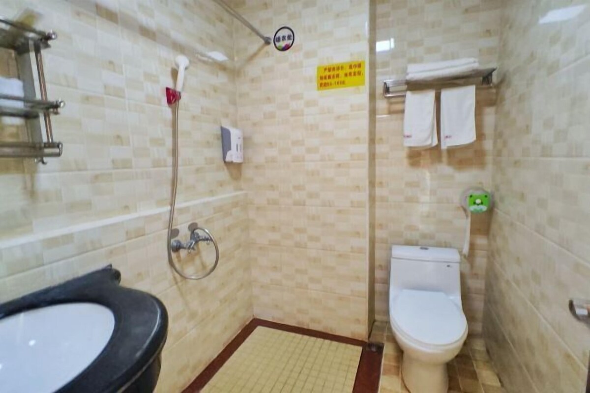 A small bathroom with a sink, toilet, and shower. There is a sign on the wall and towels hanging on the wall.