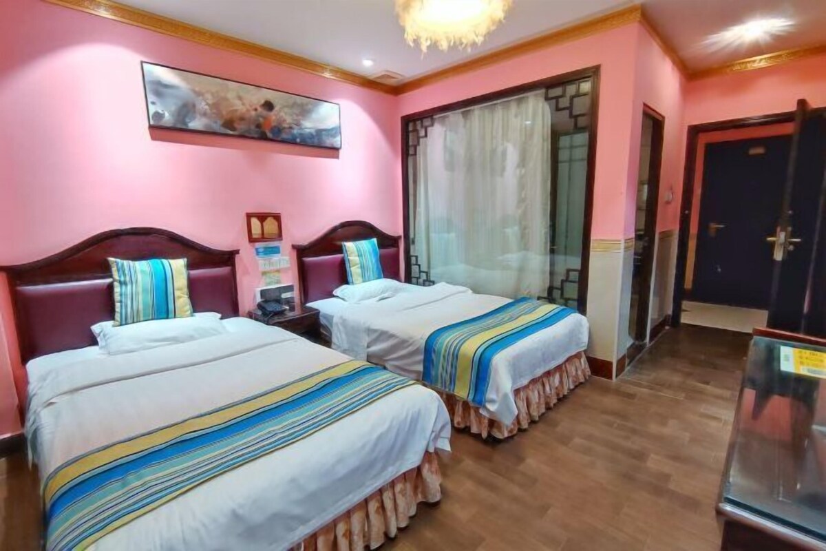 A hotel room with two beds, a large window with curtains, a painting on the wall, and a wooden floor.