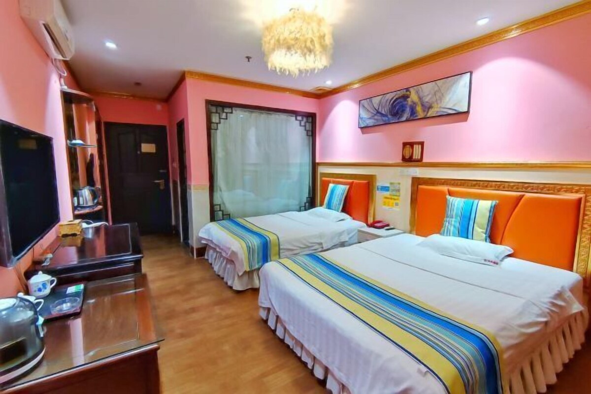 A hotel room with two beds, a desk with a computer, a television, and a chandelier.