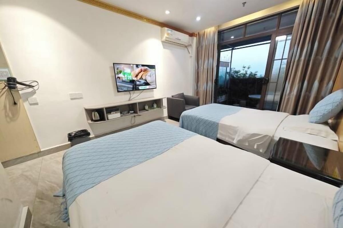 A hotel room with two beds, a TV, a desk, and a window with curtains.